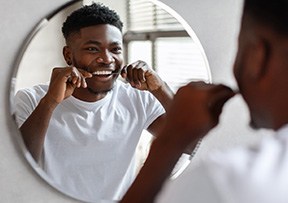 Man smiling while flossing his teeth in bathroom