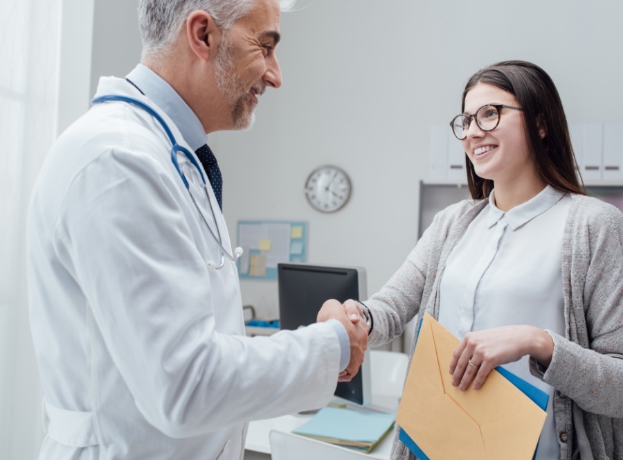 Patient holding dental insurance forms and shaking hands with dentist