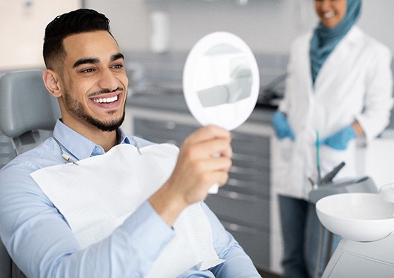 Man in dentist’s chair smiling at reflection
