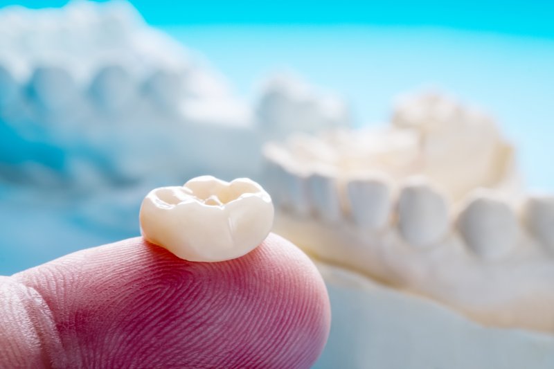 Metal free dental crown resting atop a finger with two models of jaws in the background